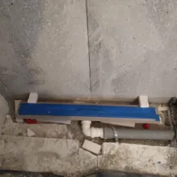 Montaż odpływu liniowego w surowej łazience, widoczne rury kanalizacyjne i fragmenty gruzu.