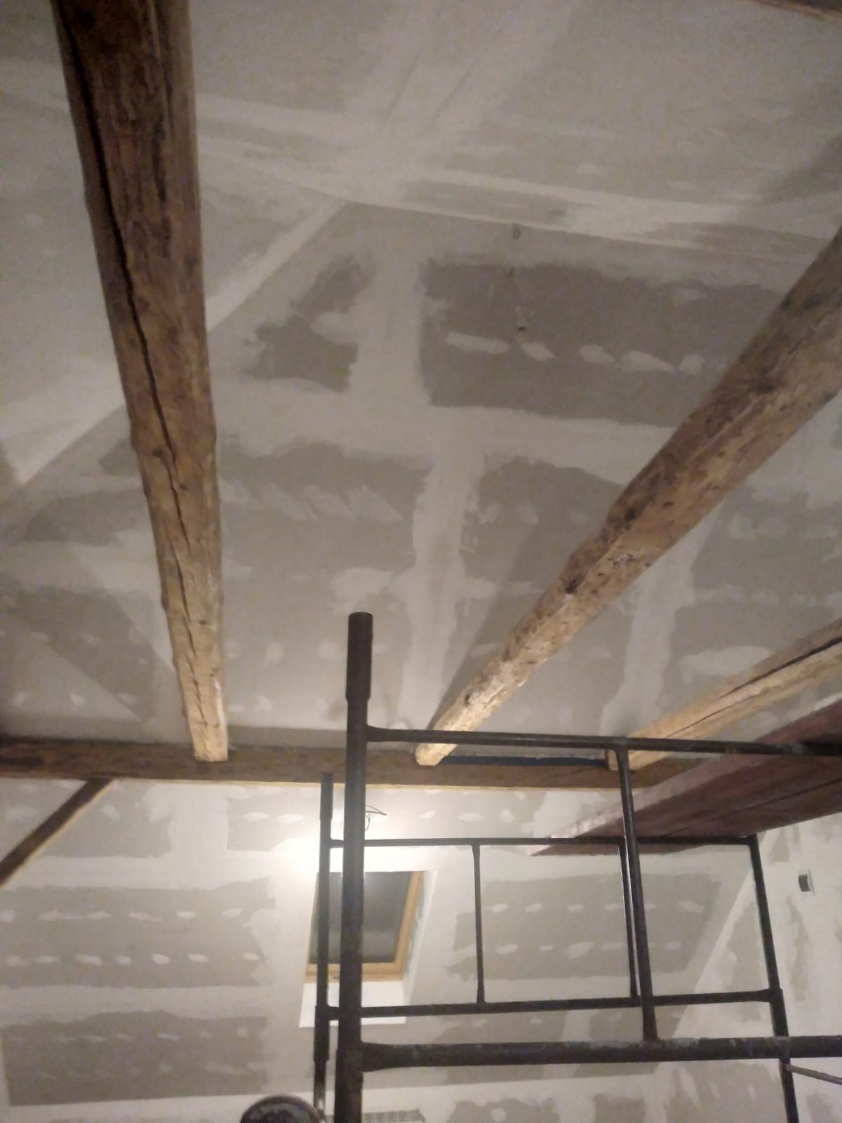 Sufit w trakcie remontu z widocznymi drewnianymi belkami i szpachlowanymi płytami gipsowymi, ustawione rusztowanie.