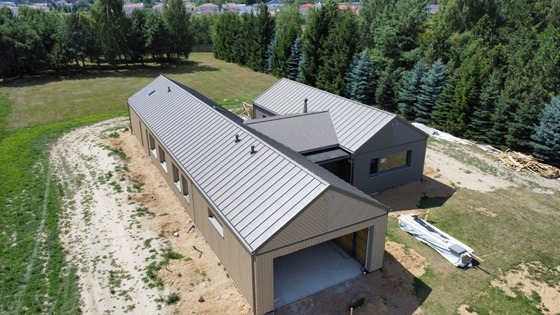 Nowoczesny, parterowy budynek z szarą blachodachówką, widok z lotu ptaka, z otwartym garażem i elementami wykończeniowymi na zewnątrz.