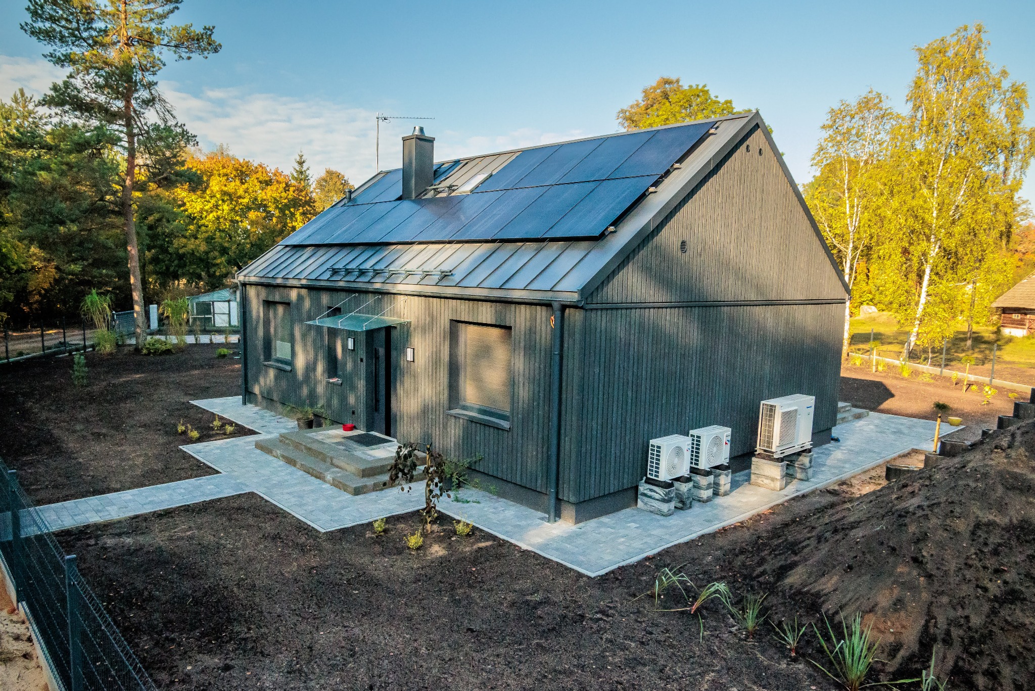 Nowoczesny, ciemny dom z panelami słonecznymi na dachu, widok z góry, świeżo ułożona kostka brukowa i klimatyzatory na zewnątrz.