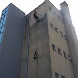 Dwóch alpinistów przemysłowych myje elewację wysokiego budynku Urzędu Morskiego w Gdyni za pomocą myjki ciśnieniowej, widoczne zacieki i strumień wody.