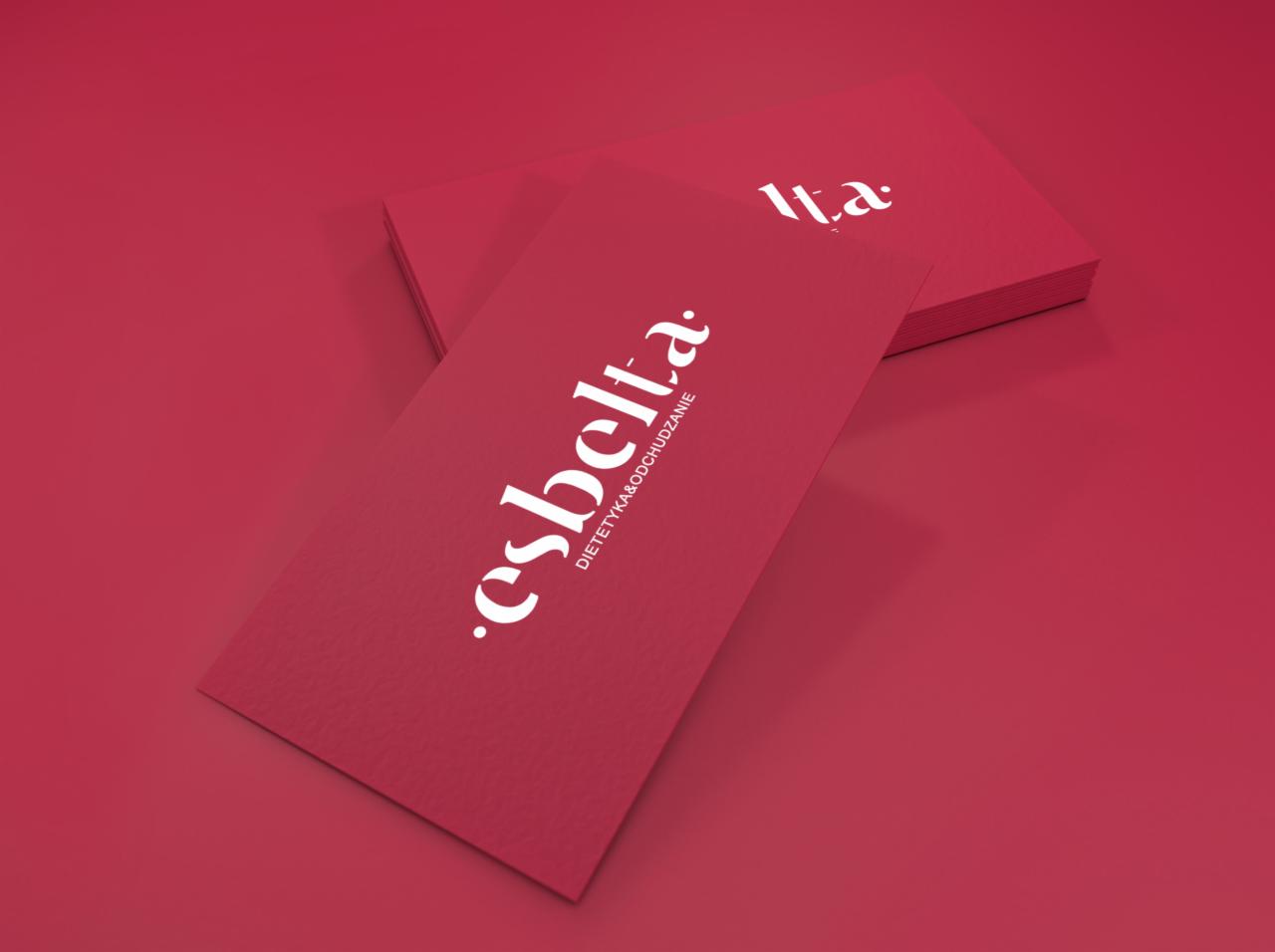 Stos wizytówek w odcieniach czerwieni z białym logo 'esbelta. DIETETYKA&ODCHUDZANIE', ułożonych pod kątem na jednolitym czerwonym tle.