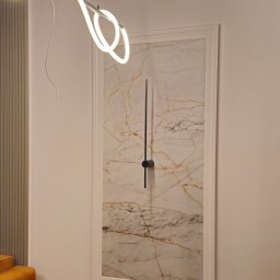 Energo-Tech Paweł Warszewski - Nowoczesne oświetlenie: abstrakcyjna lampa LED nad obrazem imitującym marmur z minimalistycznym zegarem w salonie. Elementy dekoracyjne i gniazdka elektryczne.