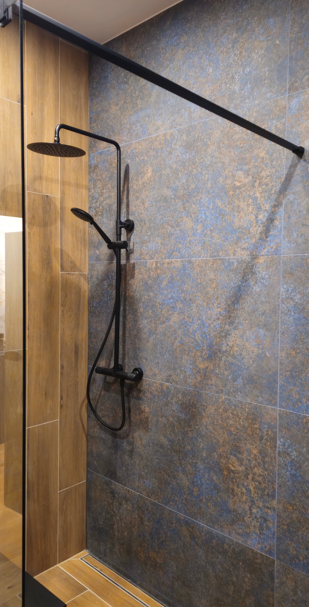 Nowoczesna kabina prysznicowa z czarną armaturą i płytkami imitującymi kamień w Poznaniu. Minimalistyczny design, widoczny odpływ liniowy i szklana ściana.