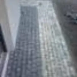 Ułożona szara kostka na podjeździe, widoczna ściana budynku po lewej stronie.