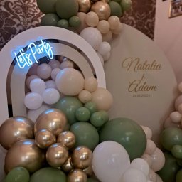 ANIMATOR Izabela Zbiega - Dekoracja balonowa w odcieniach bieli, złota i zieleni zdobiąca biały łuk z napisem neonowym 'Let's Party' oraz ściankę z imionami 'Natalia i Adam' i datą 24.06.2023, wykonana w Bochni.