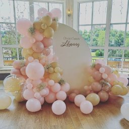 ANIMATOR Izabela Zbiega - Dekoracja balonowa w odcieniach różu i beżu z białym półokręgiem z napisem 'Chrzest Święty Lilianny', ustawiona na drewnianej podłodze przed oknami z widokiem na zieleń.