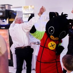 ANIMATOR Izabela Zbiega - Osoba w kostiumie Binga tańczy z gośćmi na przyjęciu, widoczna ekspresowa maszyna do kawy w tle.