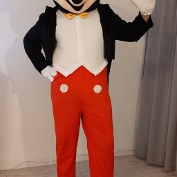 ANIMATOR Izabela Zbiega - Osoba w kostiumie Myszki Miki, ubrana w czarny frak, białą kamizelkę, żółtą muchę, czerwone spodnie z białymi guzikami i czarne kapcie, macha ręką w białej rękawiczce.