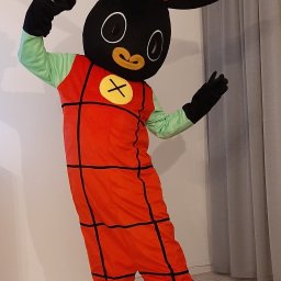 ANIMATOR Izabela Zbiega - Osoba w kostiumie królika Binga, z uniesionymi rękami, na jasnym tle ściany i zasłony.