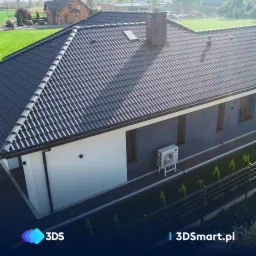 Nowoczesny dom z ciemną dachówką ceramiczną, białymi i grafitowymi ścianami oraz zewnętrzną jednostką klimatyzacji LG na metalowym stelażu.