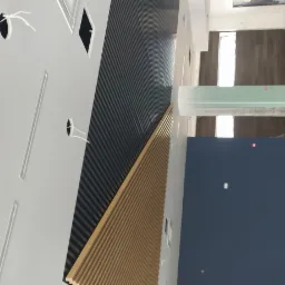 Montaż dekoracyjnych paneli ściennych z lameli w kolorze drewna i antracytu, widoczne otwory na oświetlenie w białej ścianie, surowy stan wykończenia wnętrza.