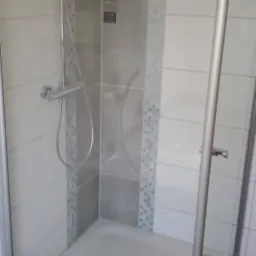 Wykończona kabina prysznicowa z szarymi i białymi płytkami, srebrną ramą i deszczownicą