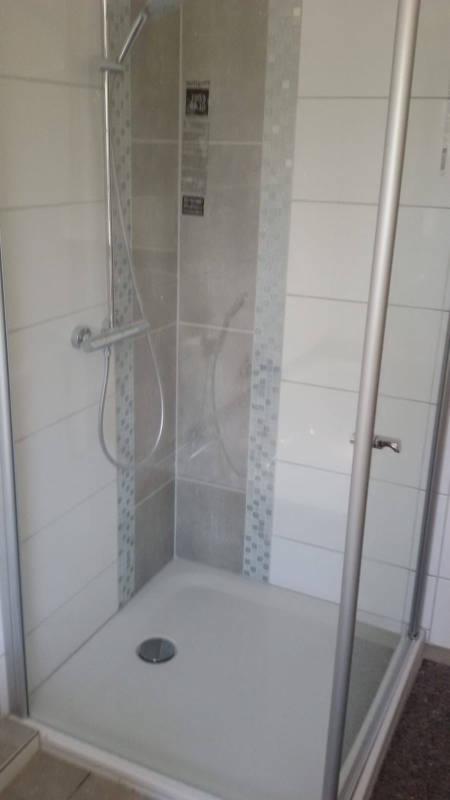 Kabina prysznicowa z odpływem liniowym, wykończona szarymi i białymi płytkami z mozaikowym akcentem na krawędziach.