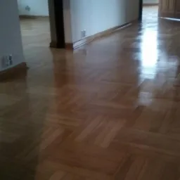 Parkiet ułożony w jodełkę, lakierowany na wysoki połysk, widoczne przejście do innego pomieszczenia.