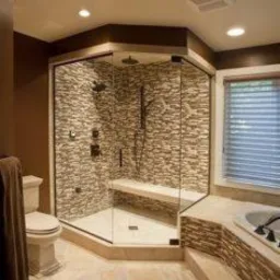 Nowoczesna kabina prysznicowa z kamienną mozaiką na ścianach, wbudowanym siedziskiem i szklanymi drzwiami, oświetlona trzema punktami świetlnymi w suficie, widok z boku na łazienkę z beżowymi...