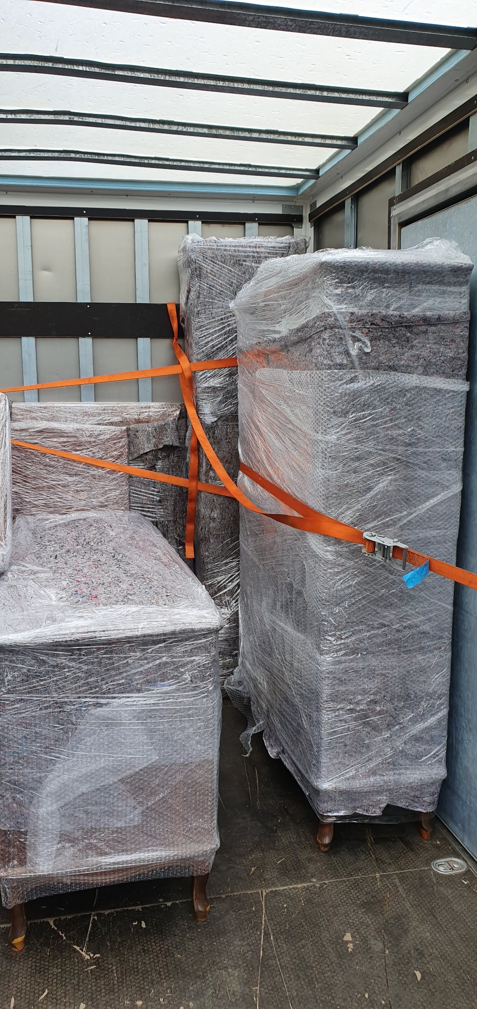 Meble zabezpieczone folią bąbelkową i pasami transportowymi wewnątrz pojazdu dostawczego.