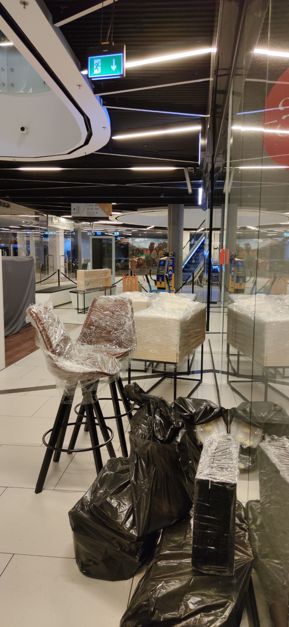 Barowe krzesła i meble biurowe owinięte folią stretch i zapakowane w czarne worki na śmieci, przygotowane do transportu w przestrzeni handlowej.