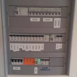 Szara rozdzielnica elektryczna Schneider z opisami obwodów, widoczne bezpieczniki i wyłączniki różnicowoprądowe, niektóre załączone, inne wyłączone, z napisem 'A.G.R. Lodówki' wykonanym markerem.