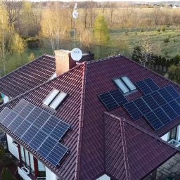 Procer Sp. z o.o. - Widok z lotu ptaka na dom z czerwoną dachówką i panelami słonecznymi, antena satelitarna na kominie, w tle drzewa i pole.