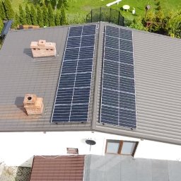 Procer Sp. z o.o. - Widok z góry na dom z brązowym dachem, na którym zamontowane są dwa rzędy paneli fotowoltaicznych, obok komina z czerwonej cegły. W tle widoczny zielony ogród.