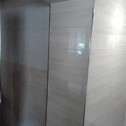 Wykończona łazienka z dwoma rodzajami płytek: strukturalnymi szarymi po lewej i gładkimi beżowymi imitującymi marmur po prawej, oddzielonymi srebrną listwą.