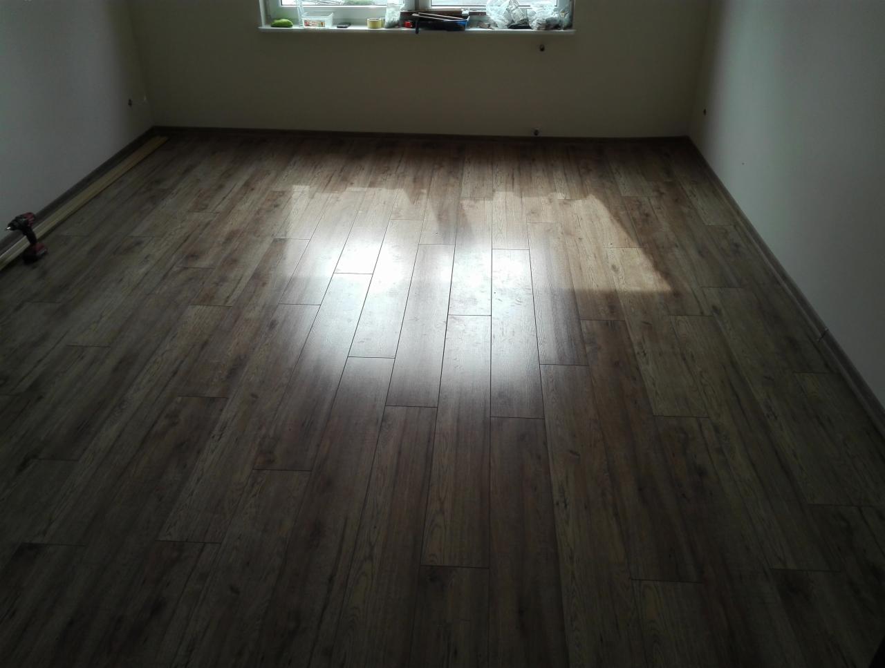 Ułożone panele podłogowe w pokoju, widoczne narzędzia i listwy przypodłogowe w trakcie montażu.