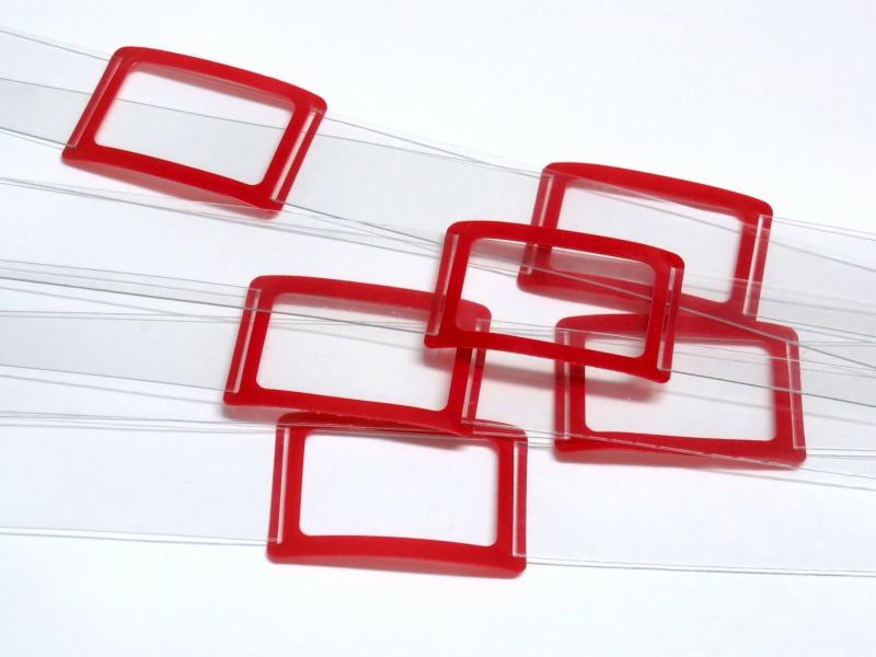 Czerwone, plastikowe ramki na przezroczystych paskach, układające się warstwami na białym tle.