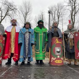 Małgorzata Kapitan-Bochner - Grupa mężczyzn w kostiumach historycznych, z tarczami i włóczniami, na scenie podczas przedstawienia plenerowego.