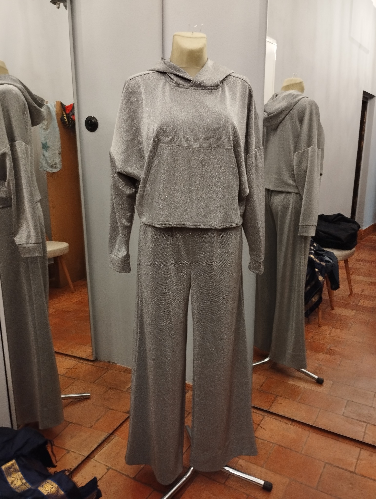 Błyszczący, srebrny dres z kapturem i szerokimi spodniami, prezentowany na manekinie w przymierzalni z lustrami.