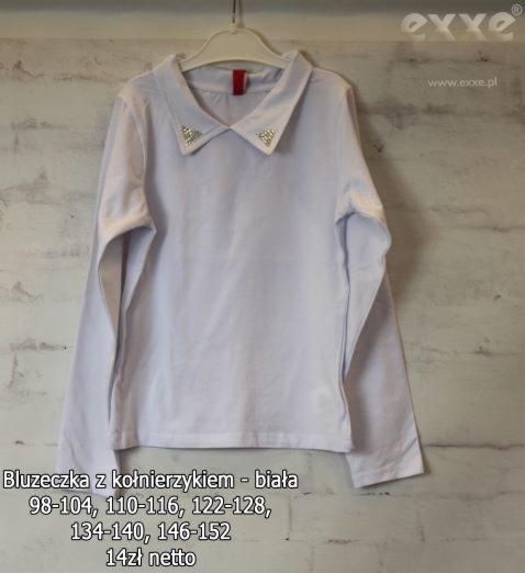 Biała bluzka z długim rękawem i kołnierzykiem zdobionym drobnymi, błyszczącymi aplikacjami, wisząca na wieszaku na tle teksturowanej ściany.