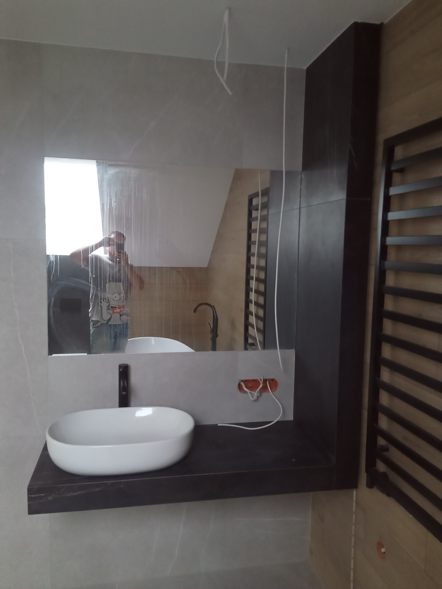 Nowoczesna łazienka w Kruszynie z owalną białą umywalką nablatową na ciemnym blacie, duże lustro z odbiciem osoby robiącej zdjęcie, widoczny fragment grzejnika drabinkowego i niezamaskowane...