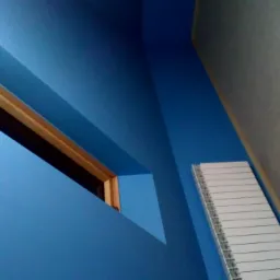 Niebieska ściana z wnęką okienną z drewnianą ramą, obok grzejnik i szara ściana, widok pod kątem.