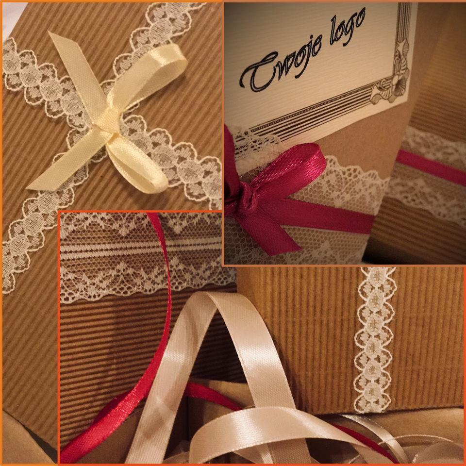 Kartonowe pudełka ozdobione koronkową tasiemką i satynowymi kokardkami w różnych kolorach, z widocznym napisem 'Twoje logo' na jednym z pudełek.