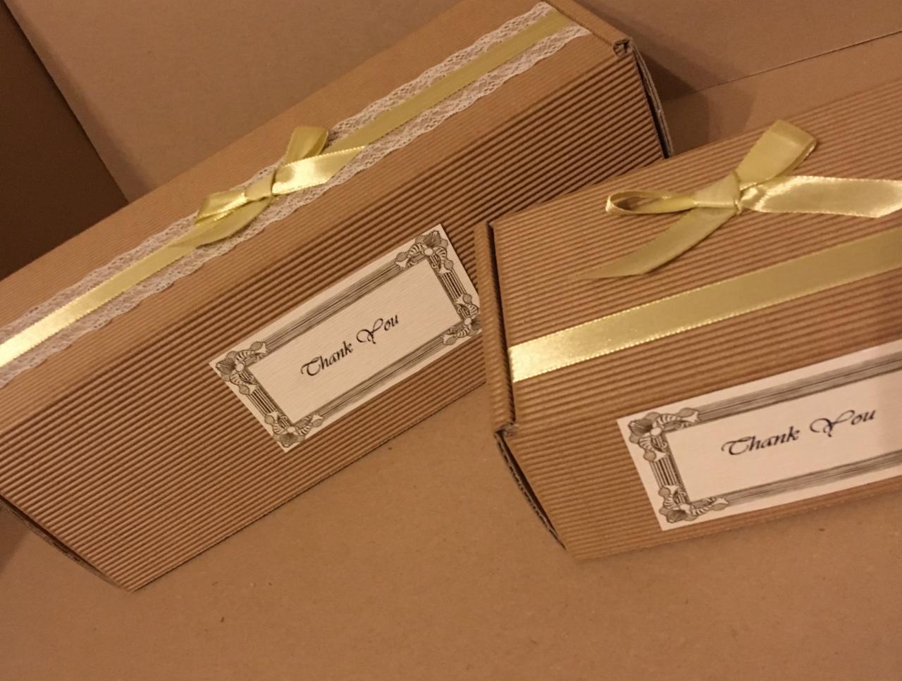 Dwa tekturowe pudełka z prążkowanej tektury, ozdobione złotymi wstążkami i etykietami z napisem 'Thank You'. Jedno pudełko ma dodatkowo koronkową tasiemkę.