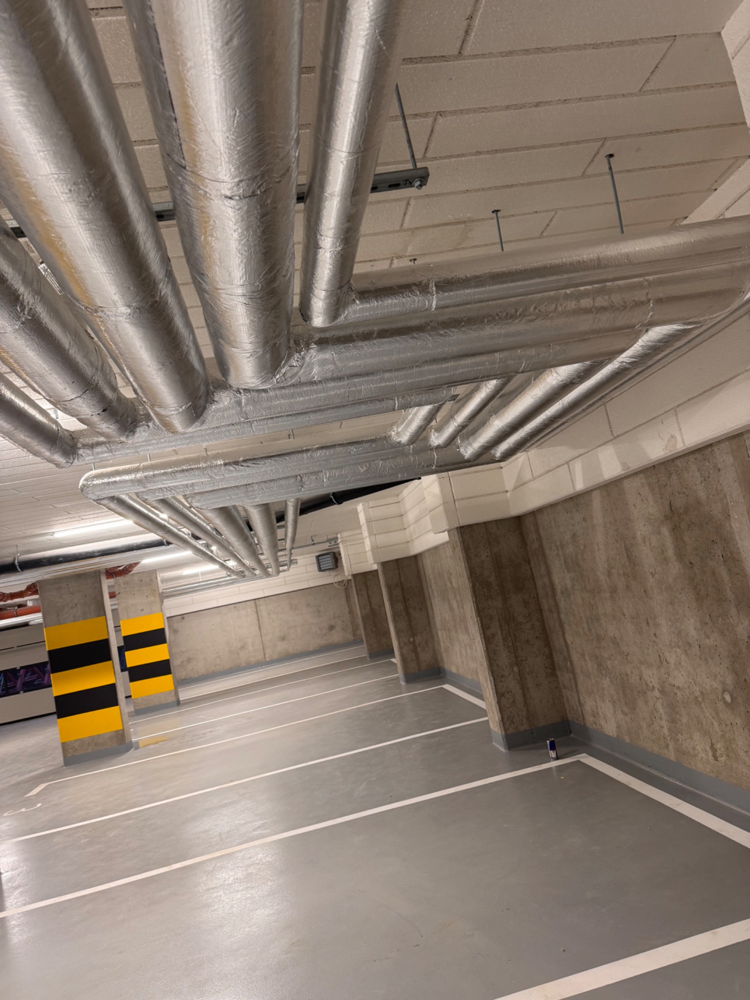 Izolowane rury pod sufitem parkingu podziemnego, widoczne elementy mocujące.