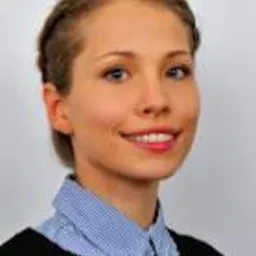 Portret kobiety z blond włosami splecionymi w warkocz, ubrana w bluzkę w paski i czarny sweter, na jasnym tle.