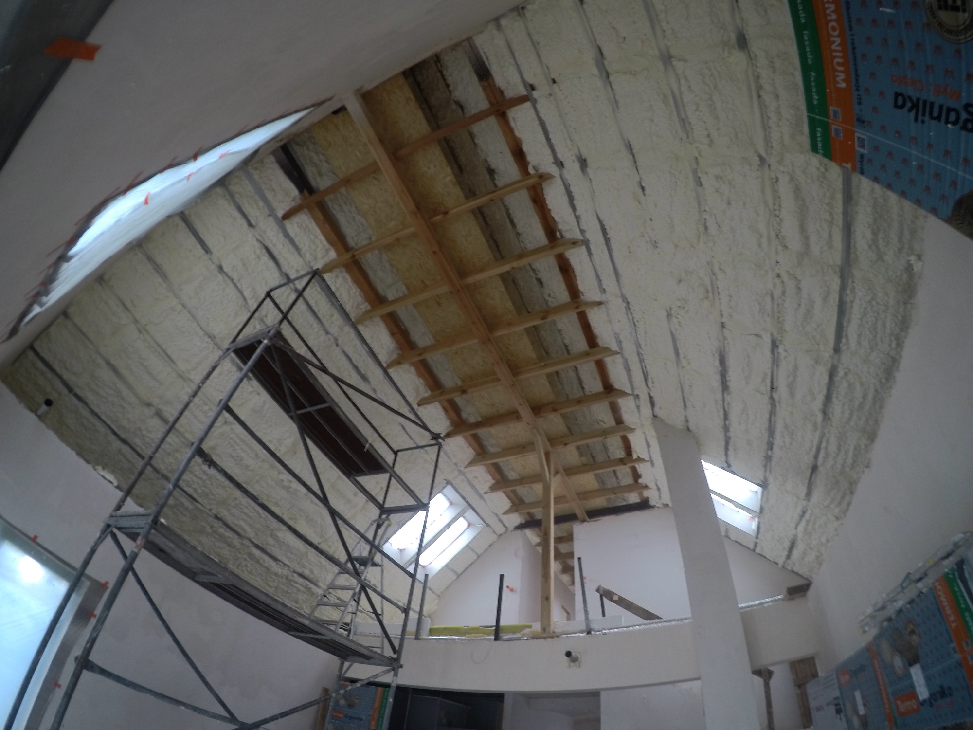Skośny strych w trakcie izolacji: pianka PUR pokrywa część powierzchni, widoczne drewniane elementy konstrukcyjne i rusztowanie.