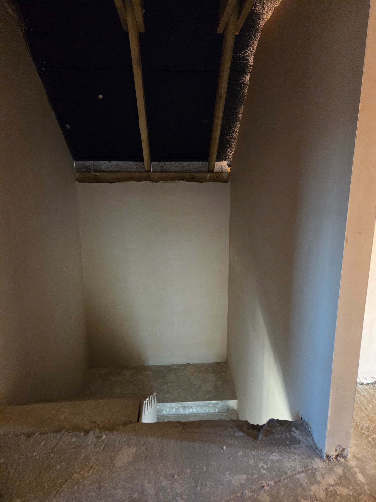 Wnętrze po tynkowaniu: gładkie ściany w surowym stanie, widoczne drewniane elementy konstrukcyjne stropu. Ujęcie z dołu schodów, podkreślające precyzję wykonania.