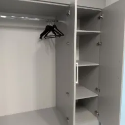 Wnętrze szarej szafy wnękowej z otwartymi drzwiami, widoczne półki, drążek na wieszaki i dwa czarne wieszaki.