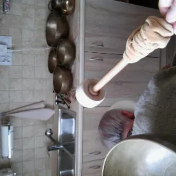 Osoba uderza pałeczką w misę dźwiękową, w tle widoczne inne misy i wyposażenie kuchni.