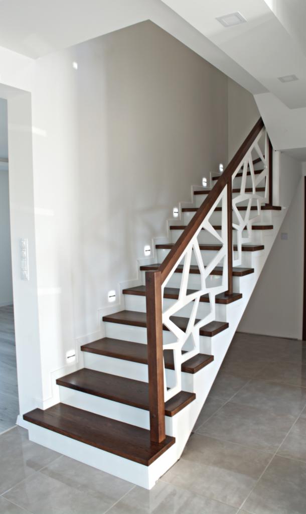 Nowoczesne schody drewniane z białymi, geometrycznymi balustradami i podświetleniem LED w stopniach, w jasnym wnętrzu.