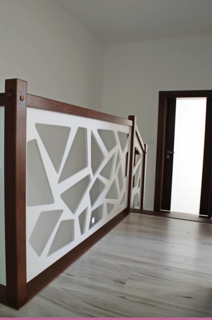 Nowoczesna antresola z białą, geometryczną balustradą i ciemnobrązowymi elementami drewnianymi, widok na podłogę z paneli i drzwi w tle.