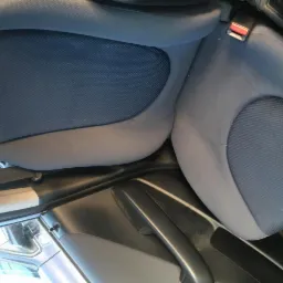 Wnętrze samochodu z widocznymi dwoma szarymi fotelami z niebieskimi wstawkami materiałowymi; na prawym fotelu leży apaszka w panterkę; widoczny pas bezpieczeństwa.