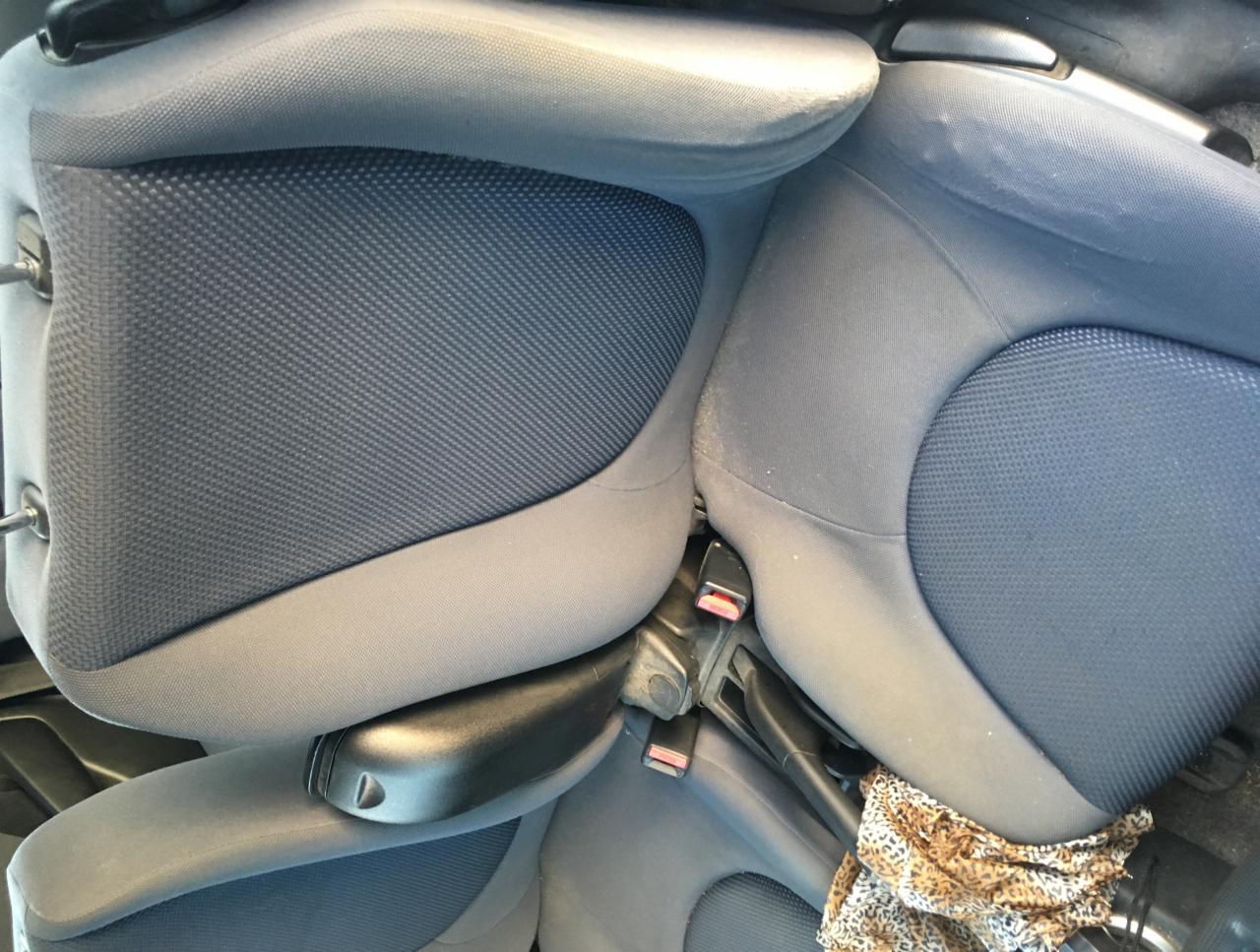 Widok z góry na wnętrze samochodu z szarą tapicerką siedzeń, widoczne zabrudzenia i fragment materiału w panterkę.