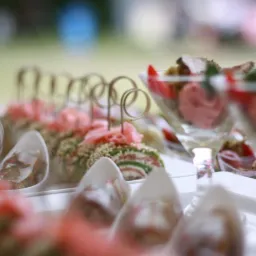 Elegancko podane przekąski na białym stole, w tym rolady z łososiem i szpinakiem oraz mini desery w szklanych pucharkach, udekorowane świeżymi ziołami i owocami.