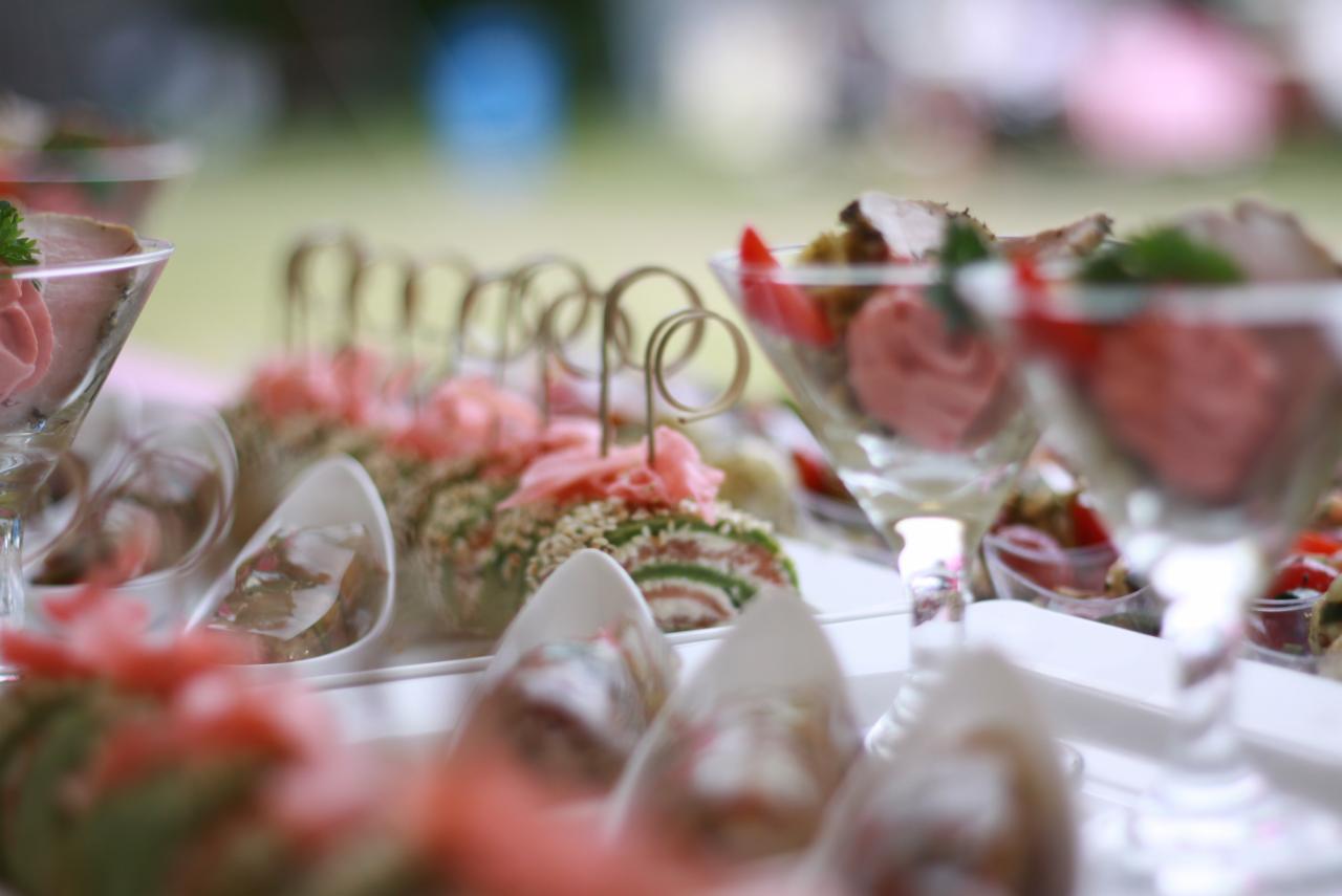 Elegancko podane przekąski na białym stole, w tym rolady z łososiem i szpinakiem oraz mini desery w szklanych pucharkach, udekorowane świeżymi ziołami i owocami.