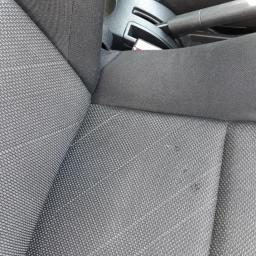 Paromax - Fragment czarnej, tekstylnej tapicerki samochodowej z widocznymi drobnymi plamami i elementami konsoli środkowej.