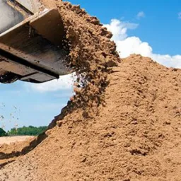 Ładowarka czołowa wysypuje piasek na pryzmę, błękitne niebo z chmurami w tle.