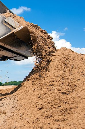 Ładowarka czołowa wysypuje piasek na pryzmę, błękitne niebo z chmurami w tle.